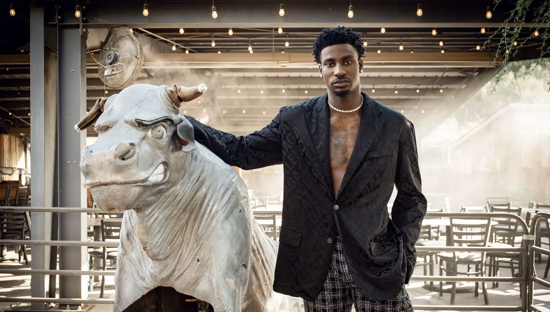 A man in a patterned blazer standing beside a large silver bull statue